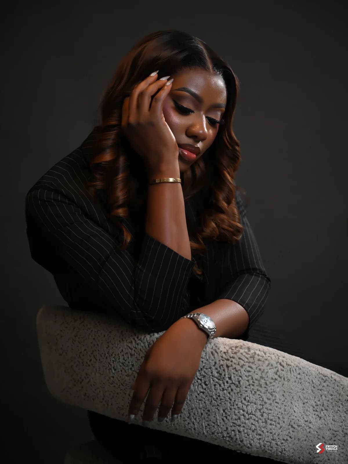Damilola leaning thoughtfully on the back of a chair in a pinstripe suit.